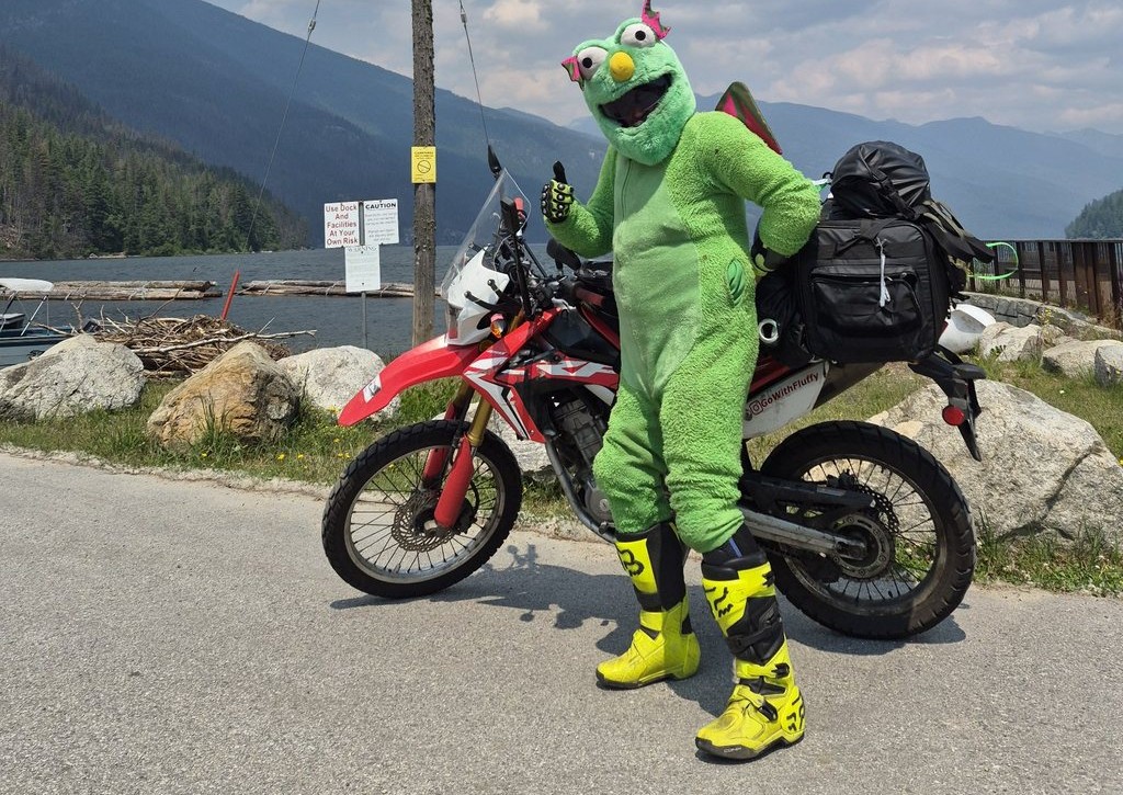 Fluffy giving a thumbs-up beside his motorcycle at a mountain lake